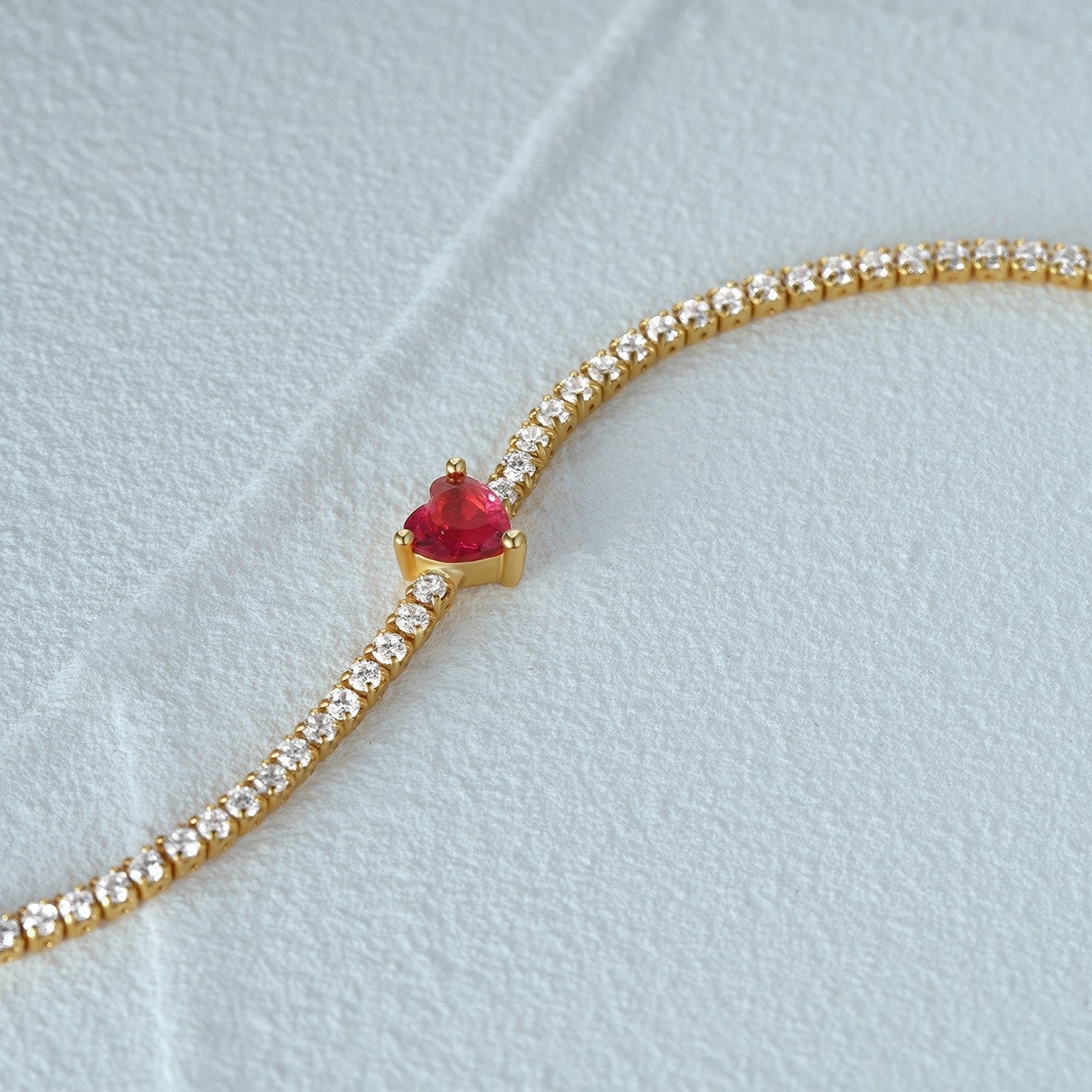 gold plated tennis bracelet with red heart-shaped crystal in the middle