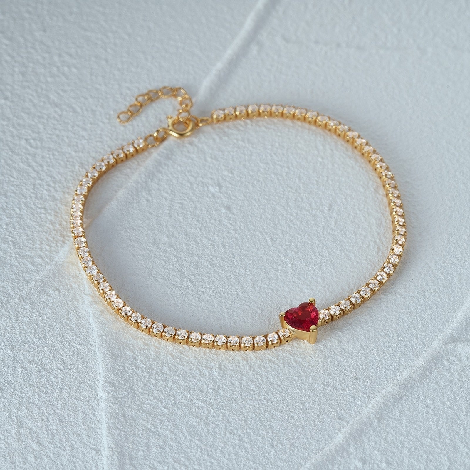 gold plated tennis bracelet with red heart-shaped crystal in the middle
