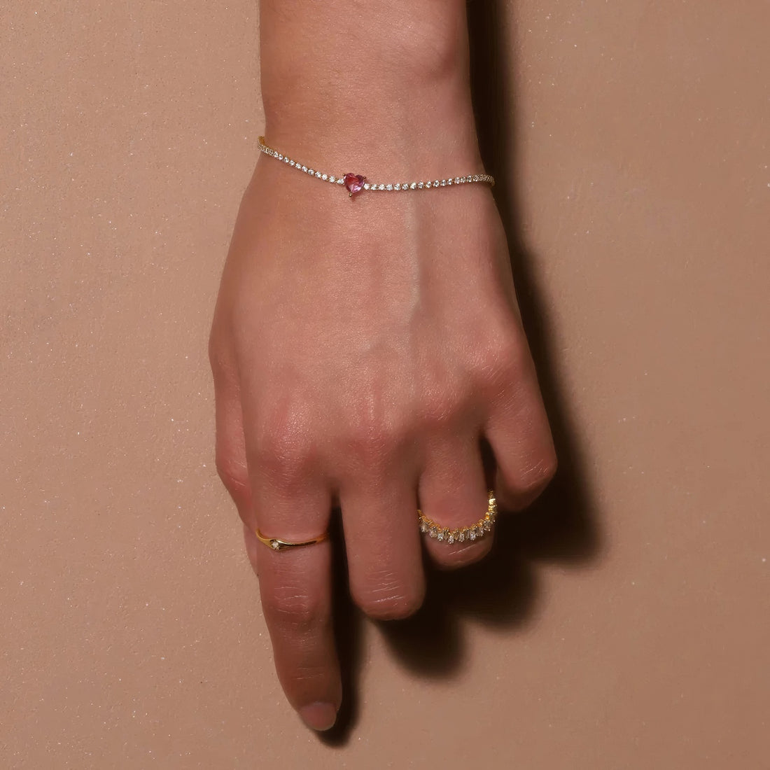 gold plated tennis bracelet with red heart-shaped crystal in the middle