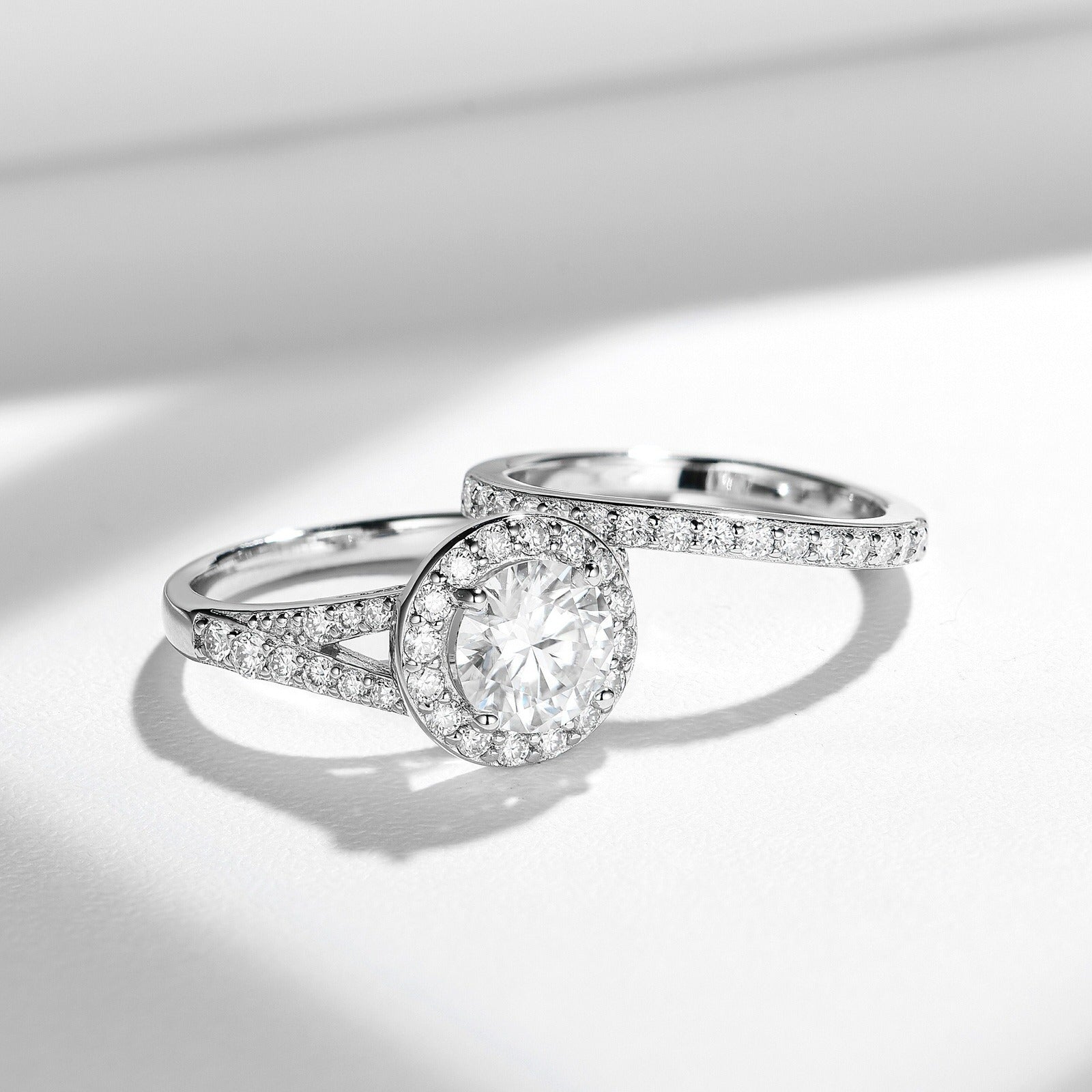 Sterling silver bridal ring set with round-cut moissanite center stone and halo, featuring a pavé split band and matching wedding band with moissanite stones