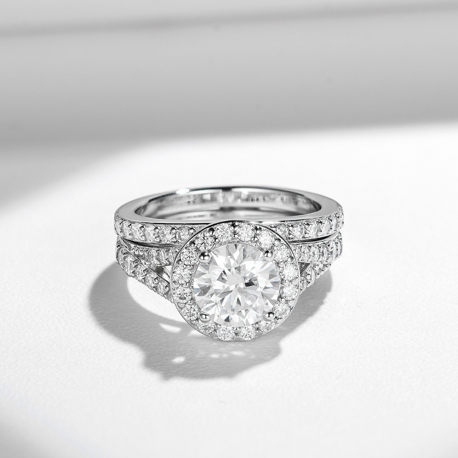 Sterling silver bridal ring set with round-cut moissanite center stone and halo, featuring a pavé split band and matching wedding band with moissanite stones