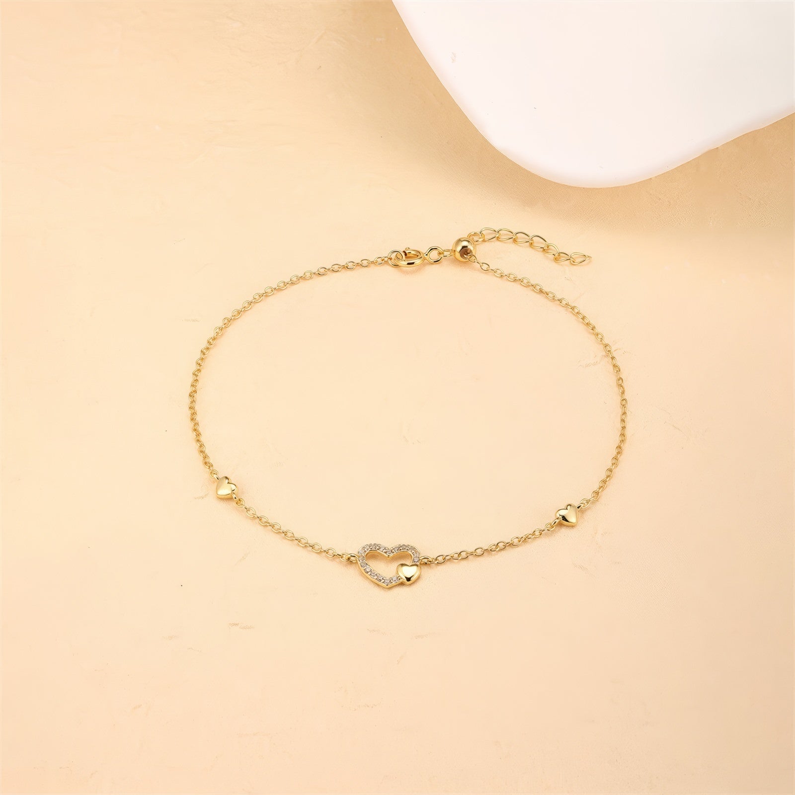 Delicate gold-plated chain bracelet featuring a central heart charm adorned with small zirconia stones, flanked by two tiny heart accents, in polished sterling silver with gold plating
