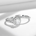 Sterling silver bridal ring set with round-cut moissanite center stone and halo, featuring a pavé split band and matching wedding band with moissanite stones