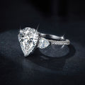 Sterling silver engagement ring with large pear-shaped moissanite center stone and heart-cut side stones, detailed with round moissanite on the band.