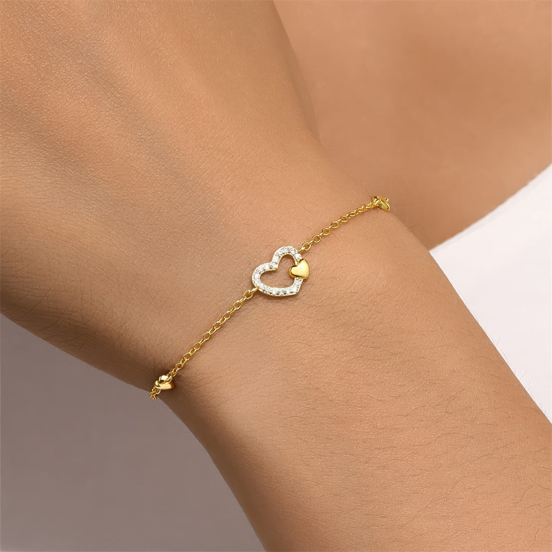 Delicate gold-plated chain bracelet featuring a central heart charm adorned with small zirconia stones, flanked by two tiny heart accents, in polished sterling silver with gold plating